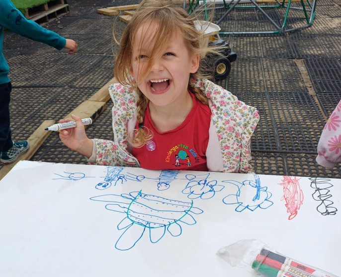 Young girl at Whitstable Day Nursery laughing and smiling while drawing pictures in the garden